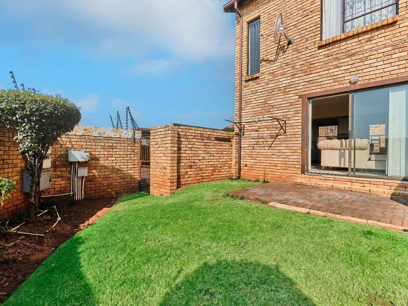 Rear garden area featuring a small paved patio, lawn, and brick boundary wall with electric fencing, accessible via a sliding glass door.