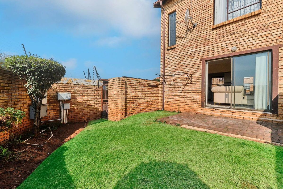 Rear garden area featuring a small paved patio, lawn, and brick boundary wall with electric fencing, accessible via a sliding glass door.