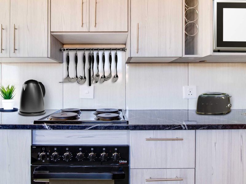 A modern kitchen featuring light wood-grain cabinetry, a dark stone countertop, an integrated electric hob, oven, and built-in microwave.