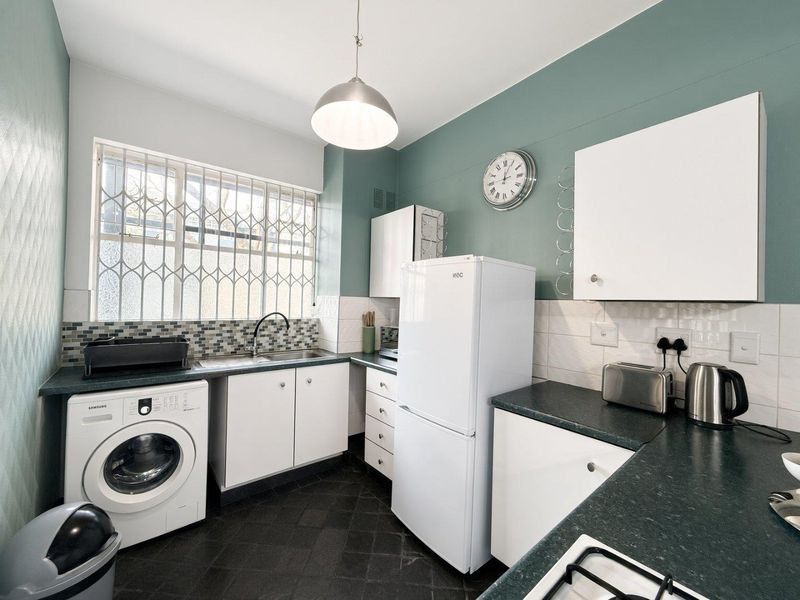 Functional kitchen featuring white cabinetry, dark laminate countertops, tiled backsplash, and integrated laundry plumbing, with security bars on the window.