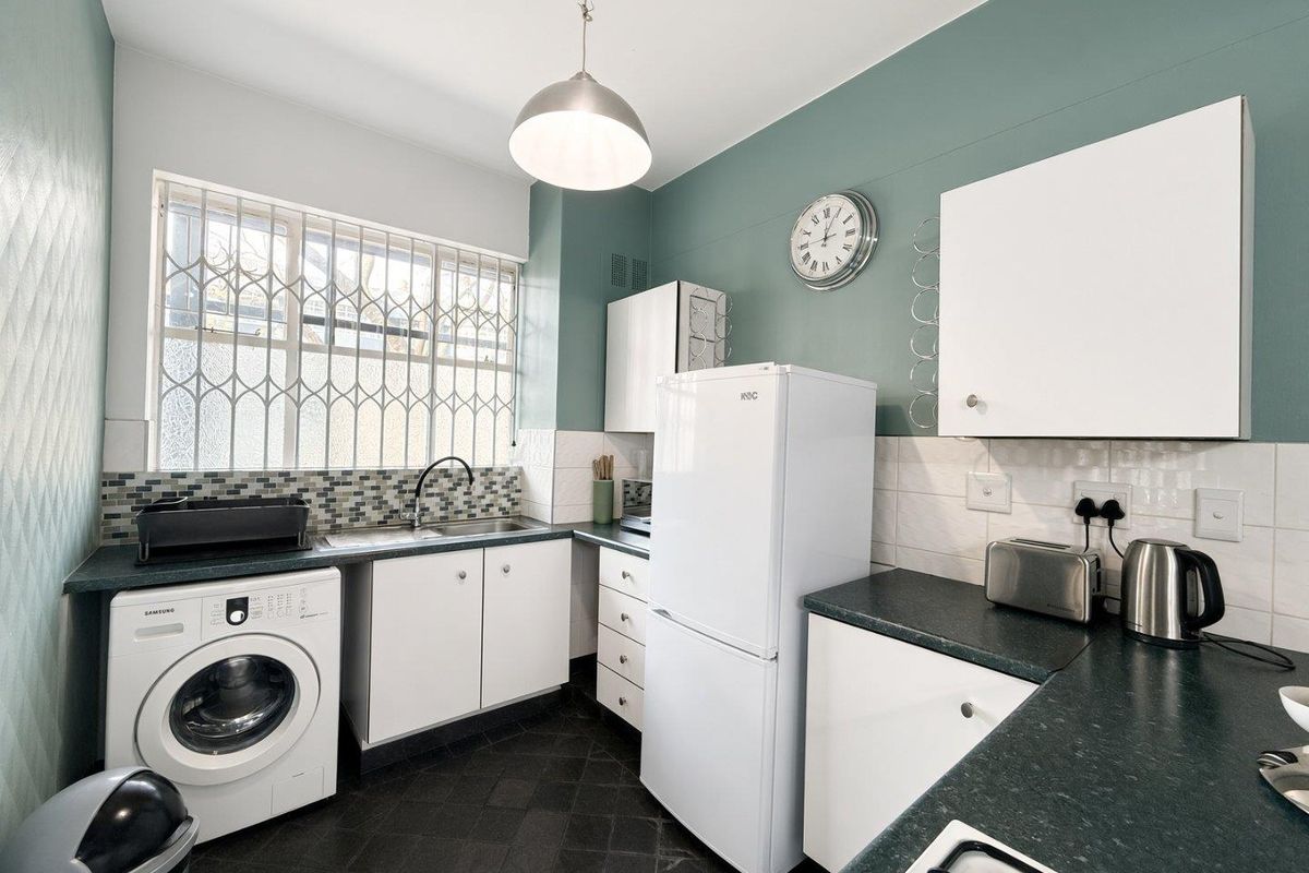 Functional kitchen featuring white cabinetry, dark laminate countertops, tiled backsplash, and integrated laundry plumbing, with security bars on the window.