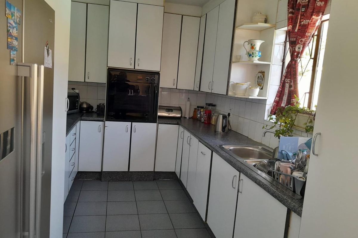 A functional kitchen featuring white cabinetry, dark laminate countertops, a built-in oven, and tiled flooring with a window providing natural light.
