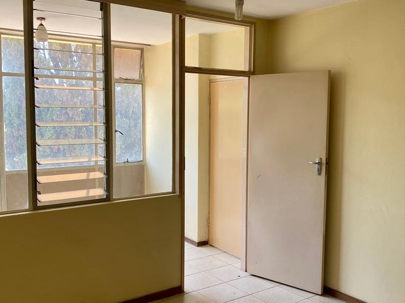 An empty living area featuring tiled flooring, an internal glass partition with louvre windows, and a standard interior door.