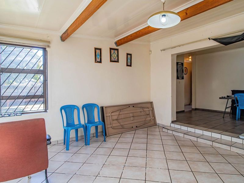 Spacious living area featuring exposed timber ceiling beams, tiled flooring, and a stepped transition to an adjacent room.