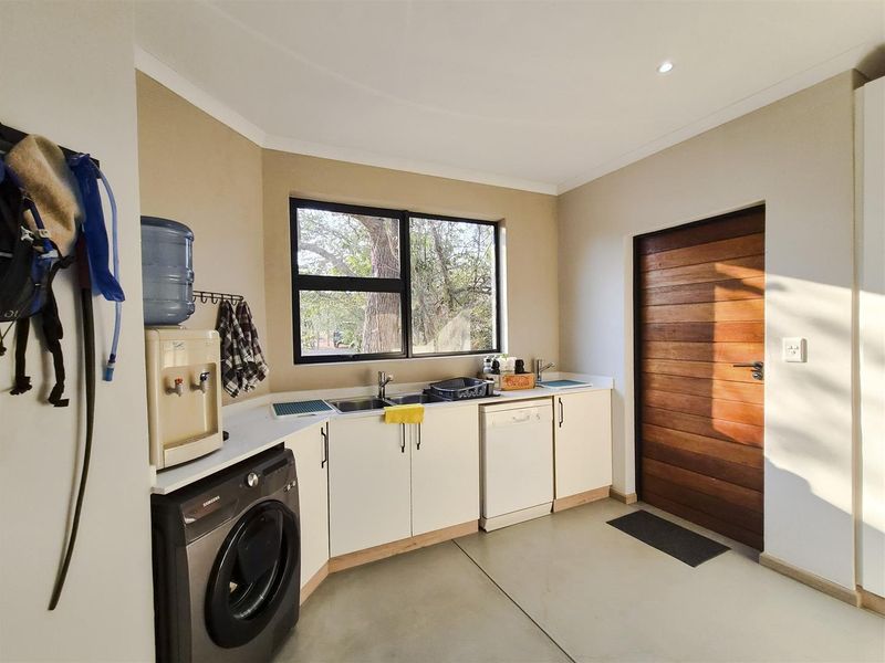 Functional laundry room featuring built-in cabinetry, stainless steel sink, and direct access to the exterior via a solid timber door.