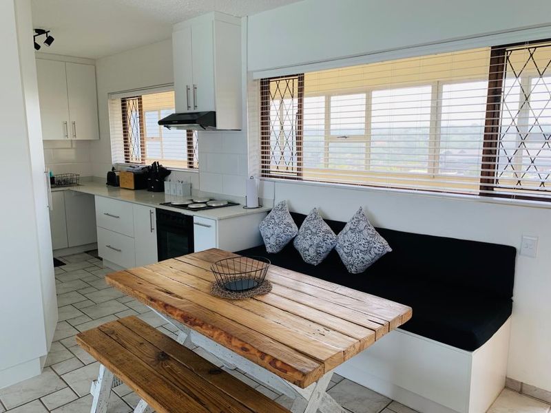 A bright, modern kitchen featuring white cabinetry, built-in oven and hob, tiled flooring, and a convenient built-in dining bench under large windows.