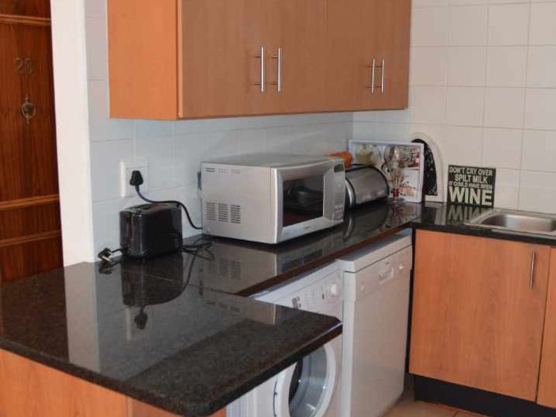 Compact kitchen featuring granite countertops, laminate cabinetry, tiled backsplash, and dedicated plumbing connections for a washing machine and dishwasher.