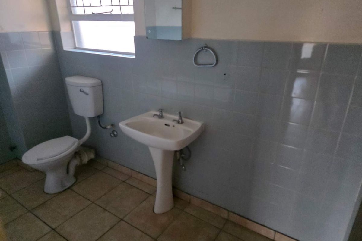 A functional bathroom featuring a pedestal sink, toilet, and tiled walls, offering a blank canvas for potential modernization and renovation.