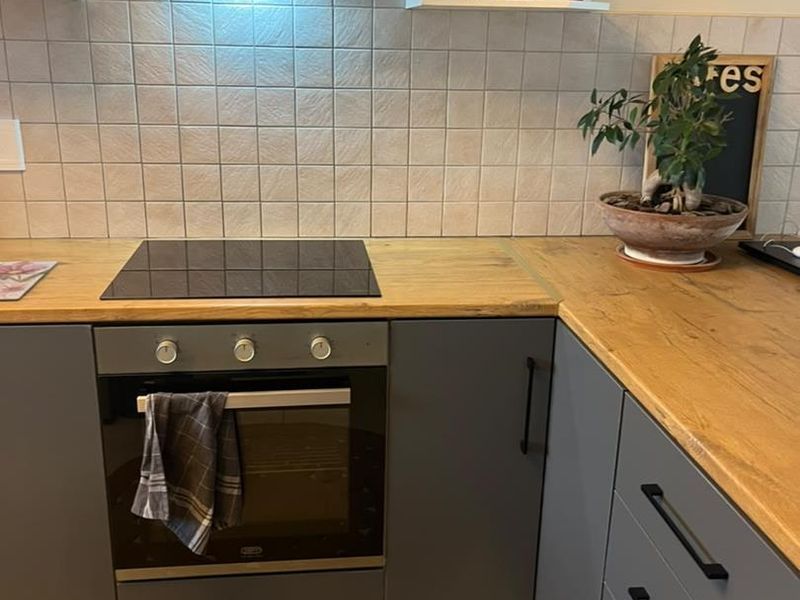 A functional kitchen featuring modern grey cabinetry, wood-look laminate countertops, a built-in oven, electric cooktop, and a tiled backsplash.