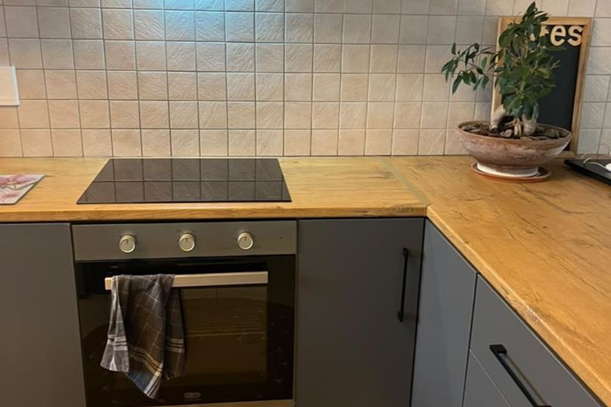 A functional kitchen featuring modern grey cabinetry, wood-look laminate countertops, a built-in oven, electric cooktop, and a tiled backsplash.