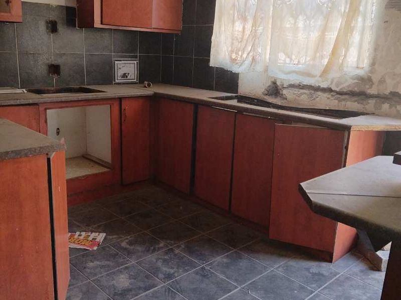 A dated kitchen featuring dark tiled flooring, dark cabinetry, and a tiled backsplash, currently in need of renovation and repair.