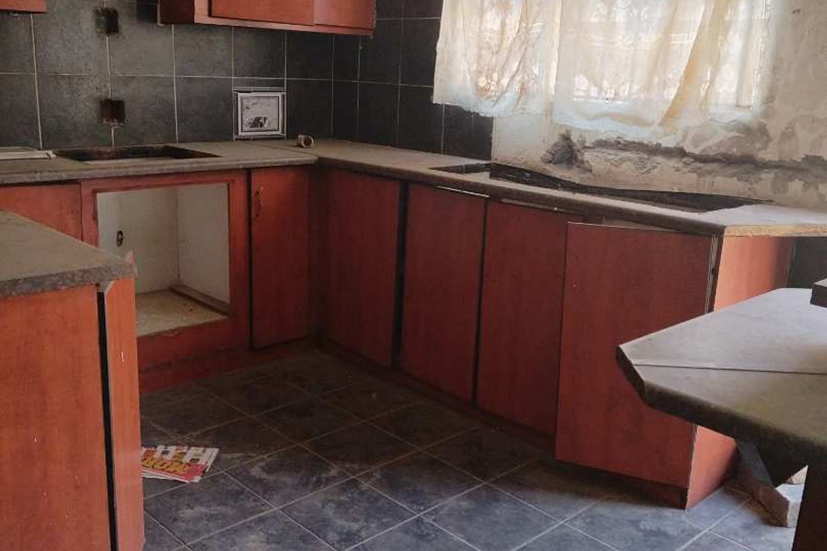 A dated kitchen featuring dark tiled flooring, dark cabinetry, and a tiled backsplash, currently in need of renovation and repair.