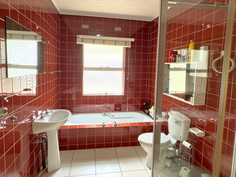 A dated bathroom featuring bold red wall tiles, a pedestal basin, a built-in bathtub, and a separate glass-enclosed shower.