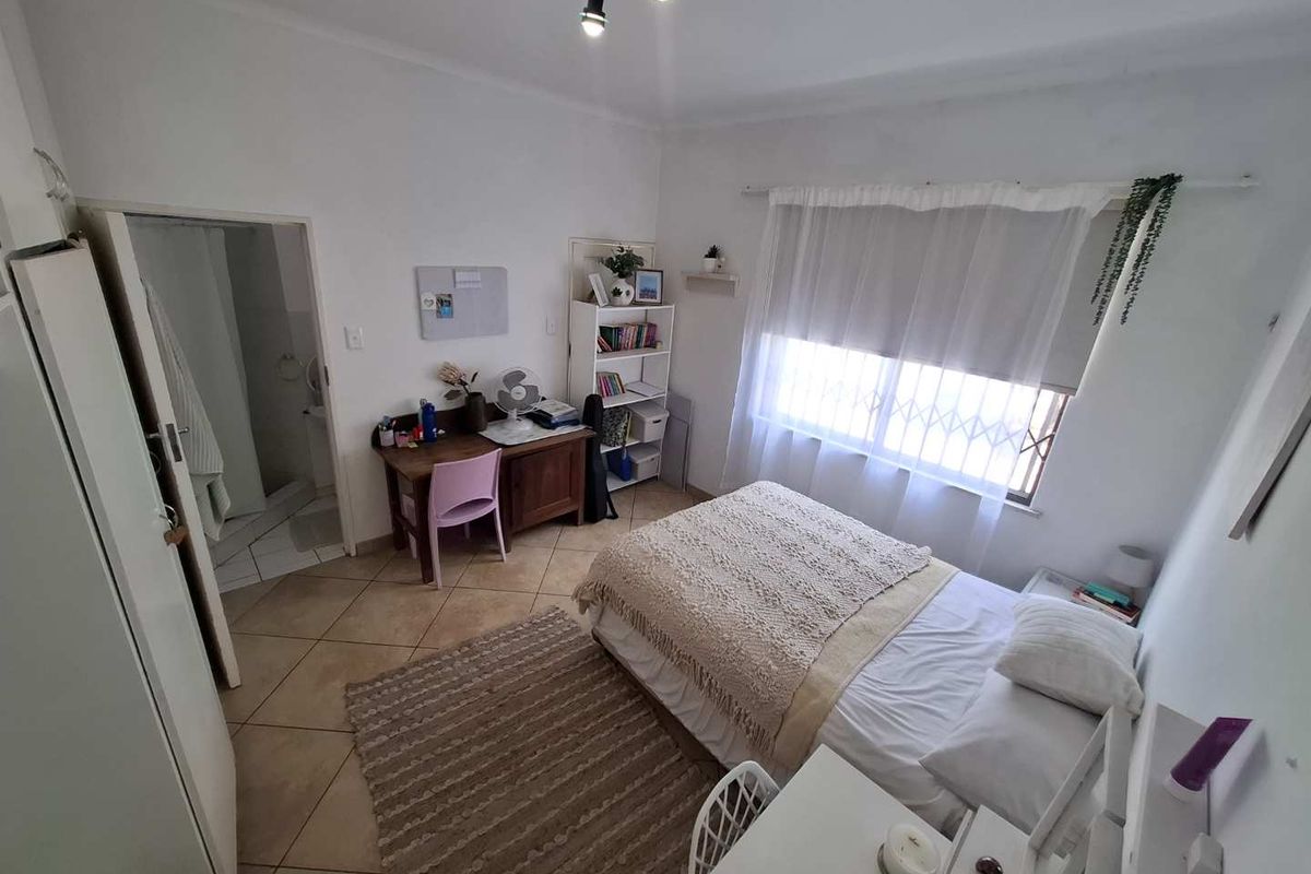 A functional bedroom featuring tiled flooring, built-in cupboards, and an en-suite bathroom access, providing a practical and comfortable living space.