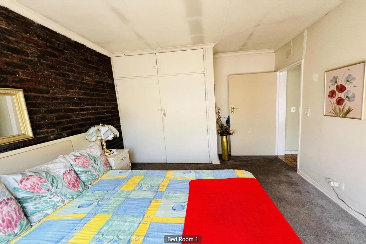 A bedroom featuring a distinctive exposed brick feature wall, built-in cupboards, and carpeted flooring.