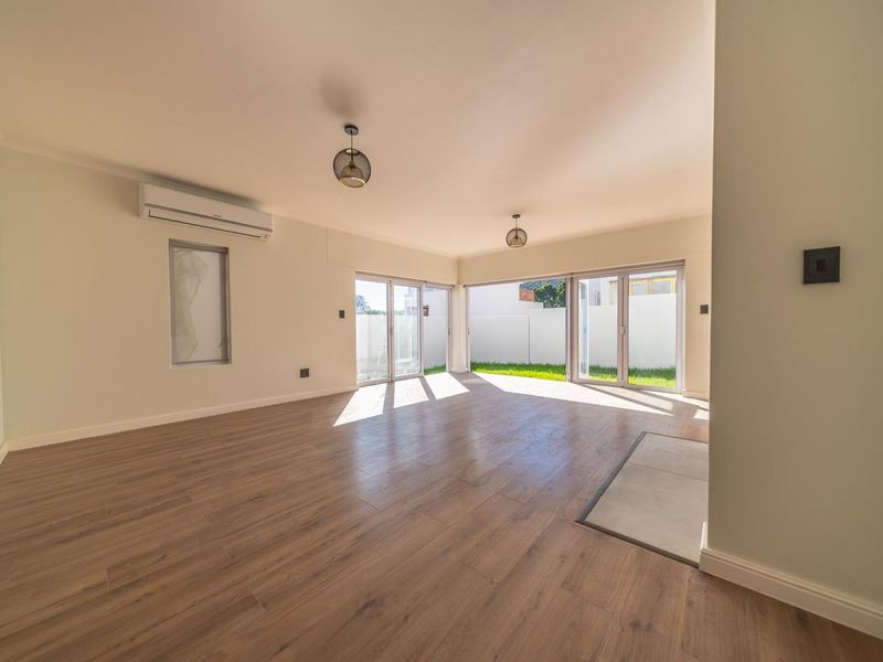 Spacious, light-filled living area featuring modern laminate flooring, a split-system air conditioner, and large sliding glass doors opening to the garden.