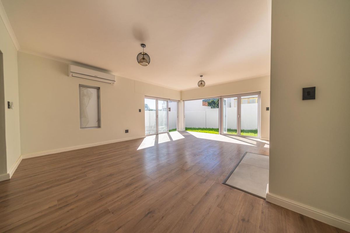 Spacious, light-filled living area featuring modern laminate flooring, a split-system air conditioner, and large sliding glass doors opening to the garden.