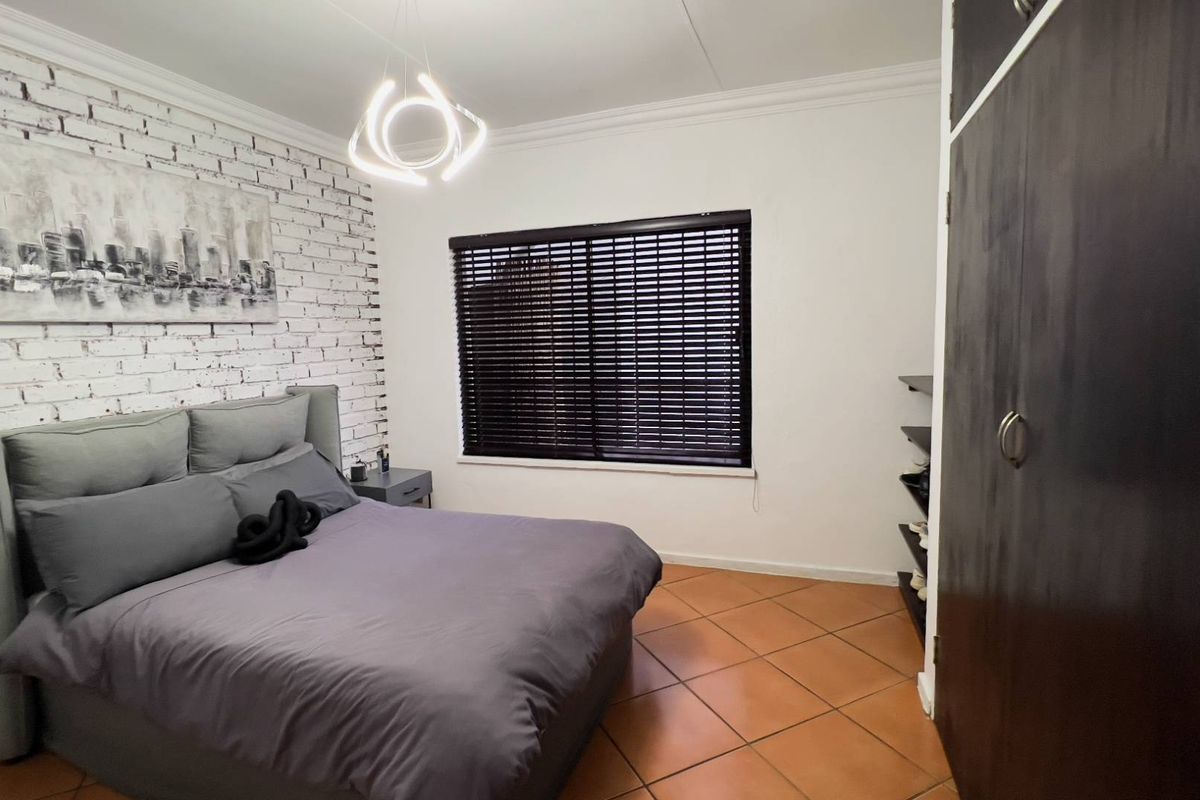 A well-maintained bedroom featuring a textured feature wall, built-in cupboards, dark tiled flooring, and modern venetian blinds.