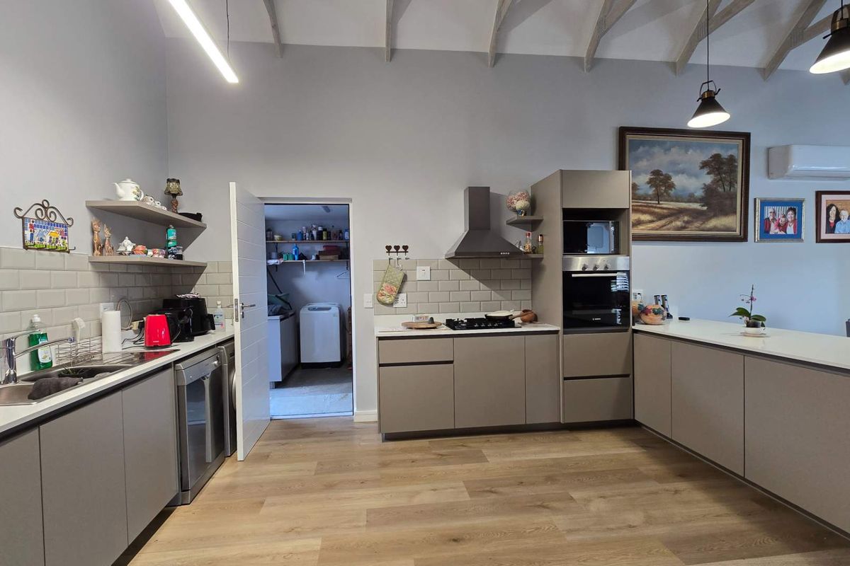 Modern kitchen featuring sleek cabinetry, subway tile backsplash, built-in appliances, and high vaulted ceilings with exposed rafters, leading into a functional scullery area.