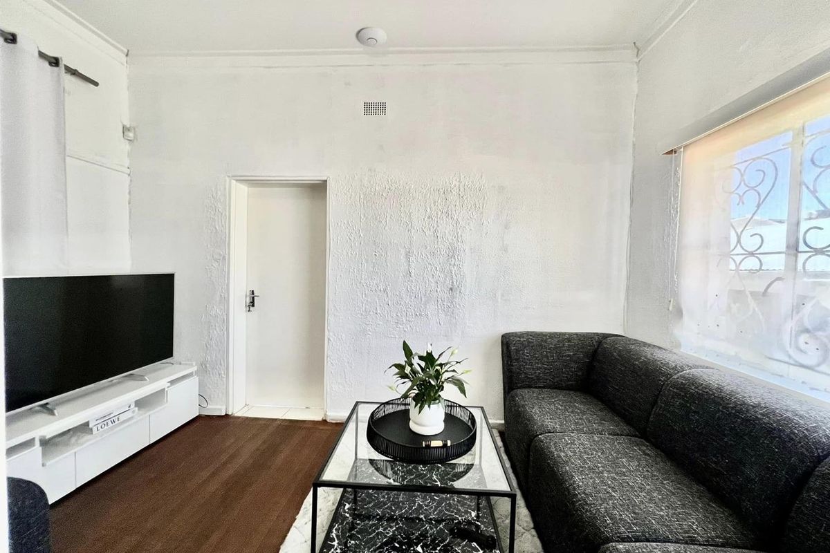 A living room featuring textured white walls, dark wood-look flooring, and a window with security bars.