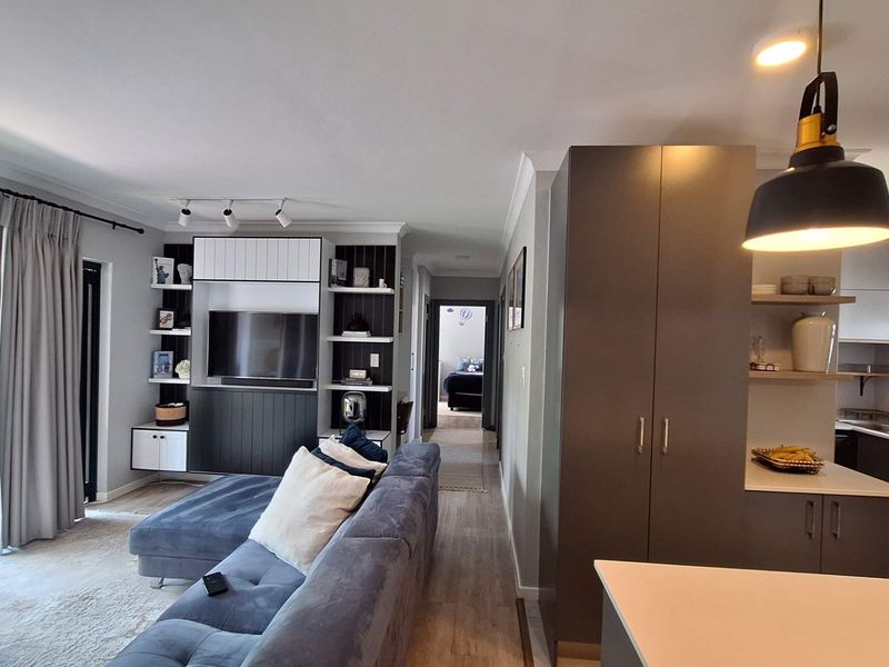 Modern open-plan living area featuring a contemporary kitchen with built-in cabinetry, laminate flooring, and seamless access to a private balcony.