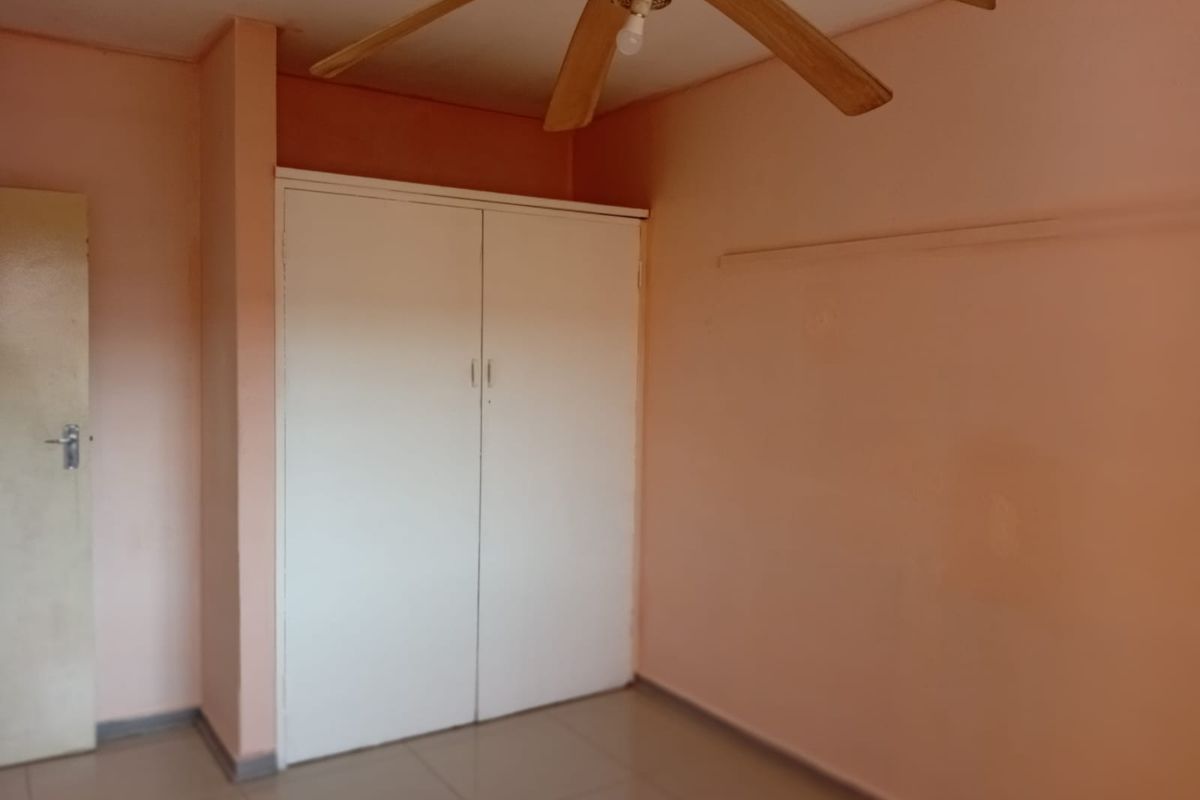 A simple bedroom featuring tiled flooring, a built-in wardrobe, and a ceiling fan, offering a blank canvas for potential updates.