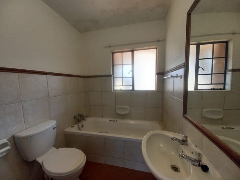 A dated bathroom featuring a bathtub, pedestal basin, and toilet, with tiled walls and floor. The space requires cosmetic updates and ceiling repairs.
