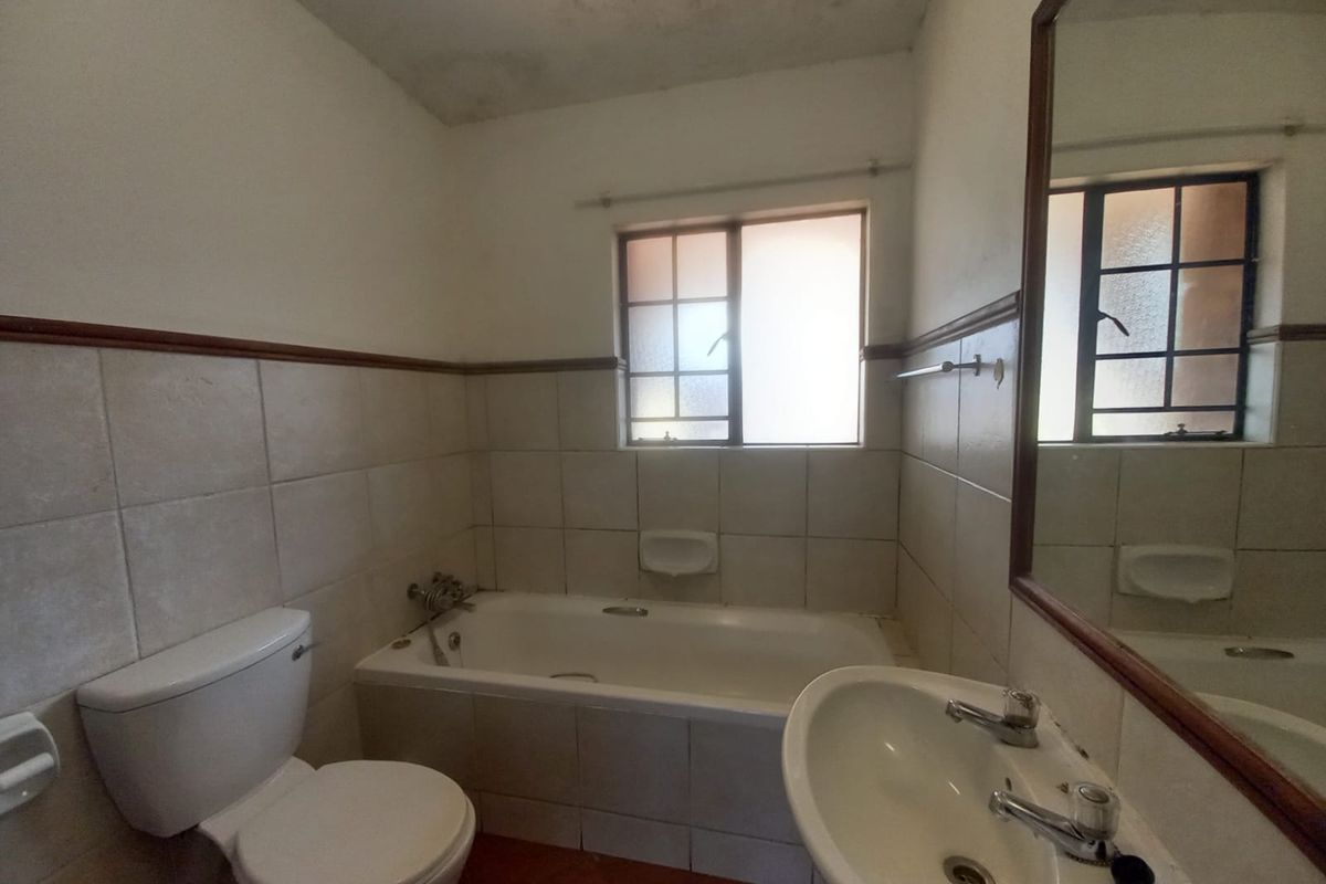 A dated bathroom featuring a bathtub, pedestal basin, and toilet, with tiled walls and floor. The space requires cosmetic updates and ceiling repairs.
