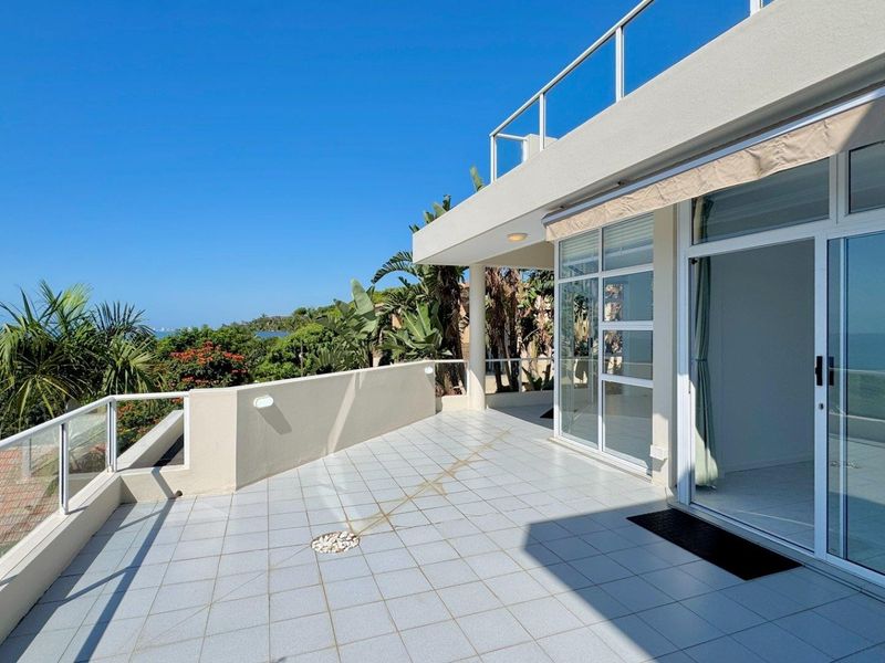 Spacious balcony featuring tiled flooring, a glass balustrade, and a retractable awning, offering expansive outdoor space with direct access to the interior.