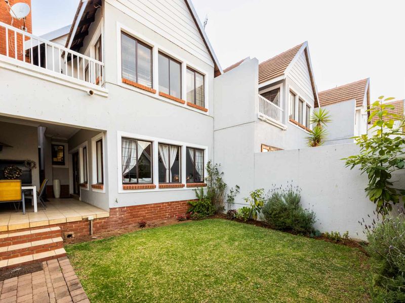 Rear view of the townhouse featuring a private garden, a paved patio area, and an upper-level balcony with white railings.