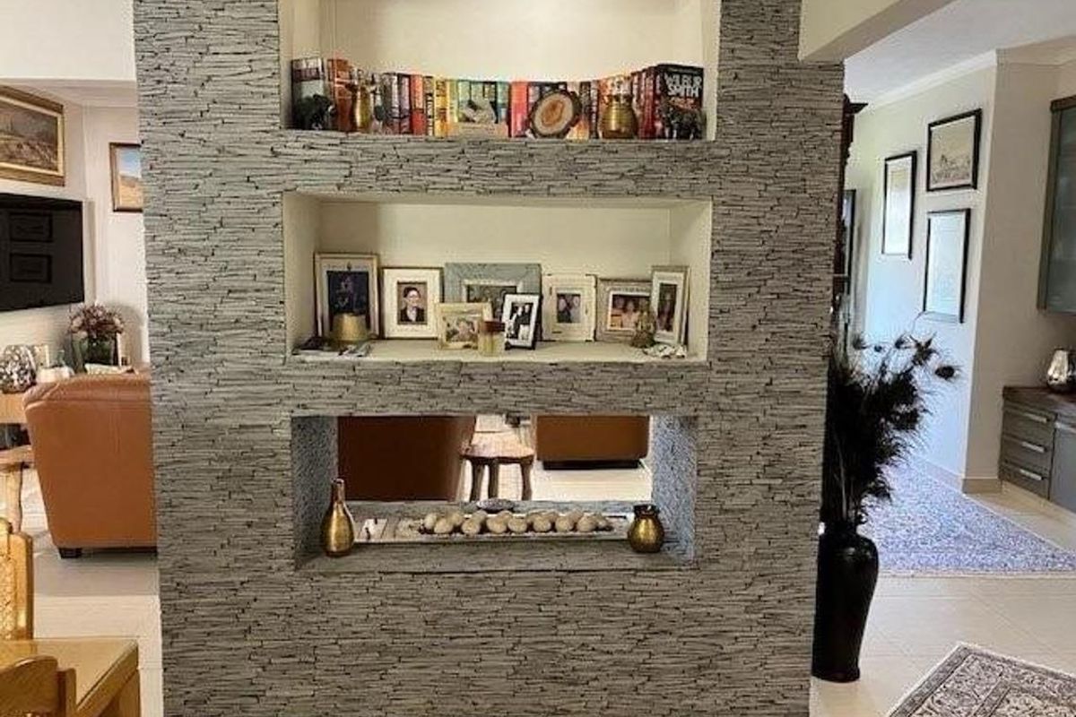A central feature wall with built-in stone-clad shelving, acting as a decorative room divider between the living and dining areas.