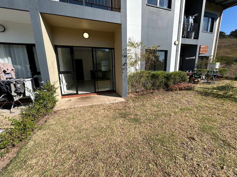 Rear view of the apartment featuring a paved patio area with sliding door access and a private garden space.