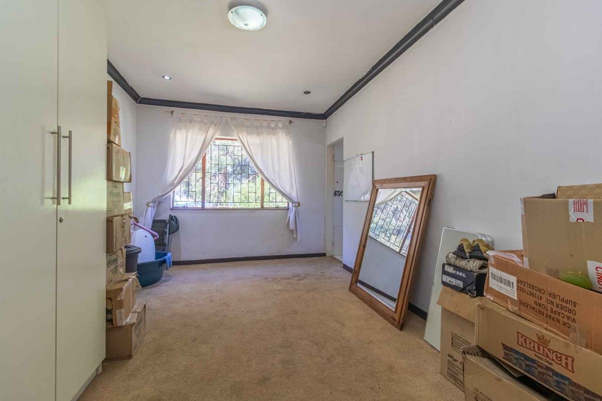 A spacious bedroom featuring built-in cupboards, carpeted flooring, and security burglar bars on the window.