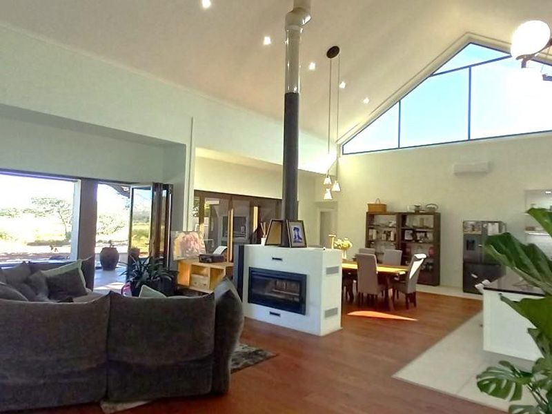 Spacious open-plan living area featuring a vaulted ceiling, central fireplace, timber flooring, and large bi-fold doors opening to an outdoor patio.