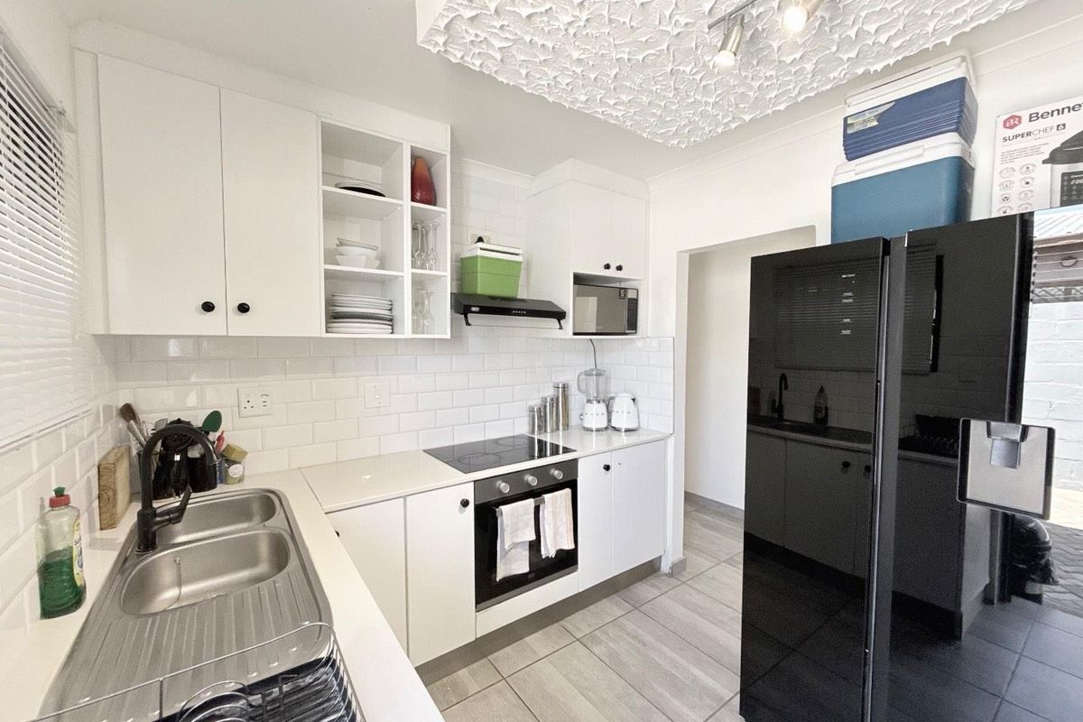 A modern kitchen featuring white cabinetry, subway tile backsplash, integrated oven and hob, and a double stainless steel sink with a matte black faucet.