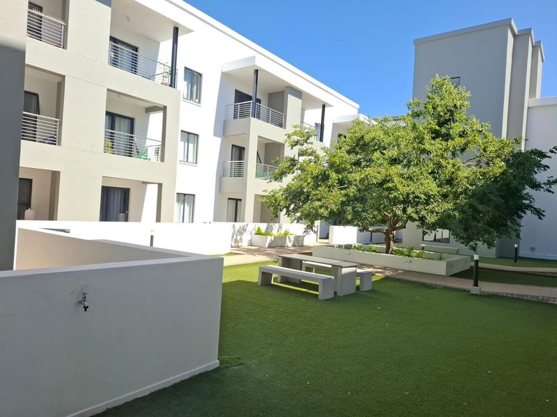 A well-maintained communal courtyard area featuring artificial lawn, raised garden beds, and access to apartment balconies.