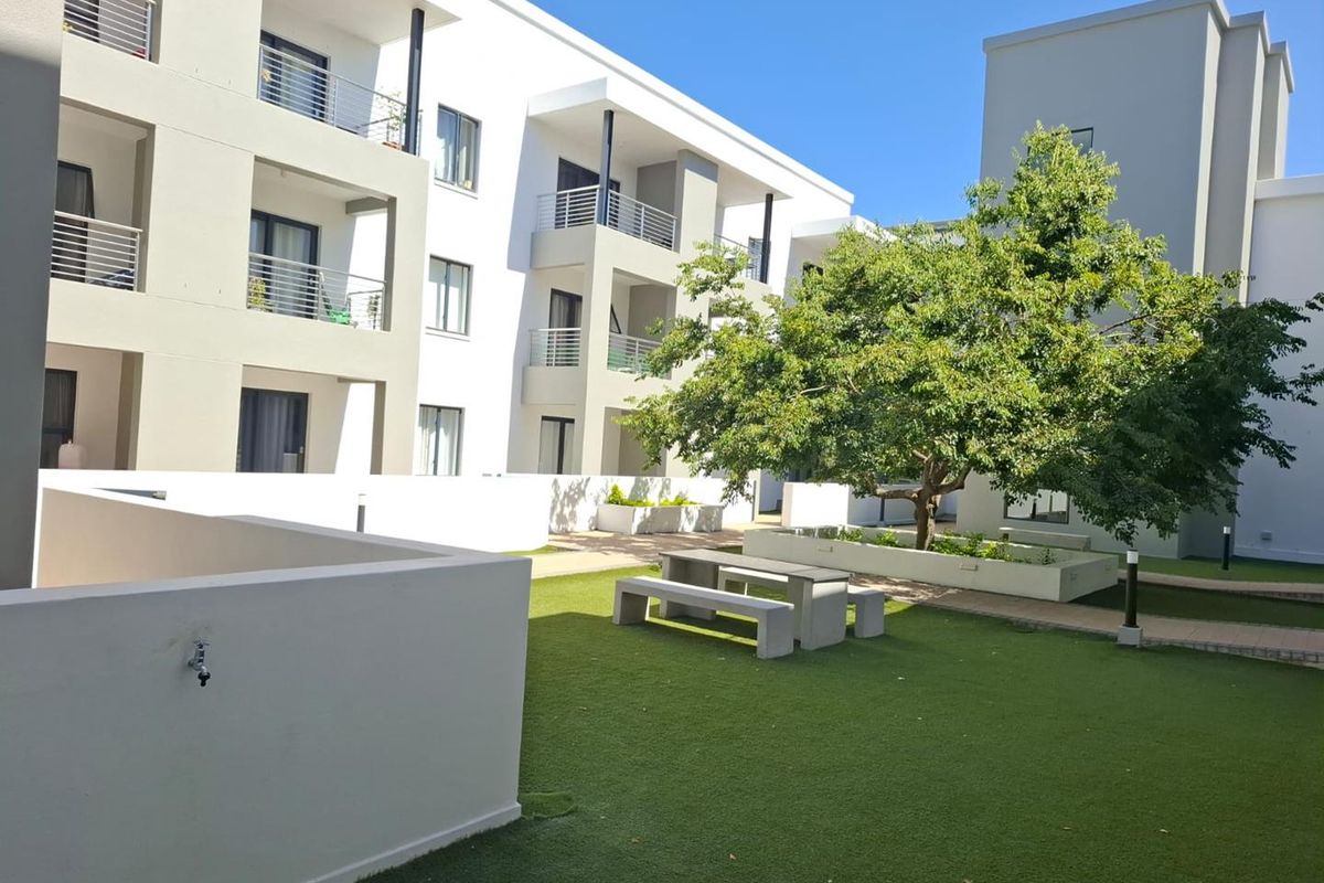 A well-maintained communal courtyard area featuring artificial lawn, raised garden beds, and access to apartment balconies.