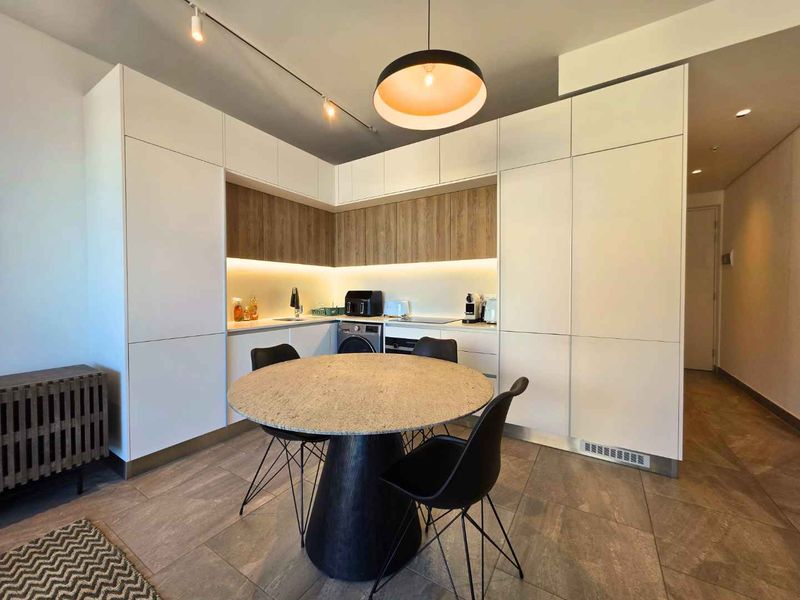 Modern open-plan kitchen area featuring sleek white cabinetry, wood-tone accents, integrated appliances, and contemporary track and pendant lighting.