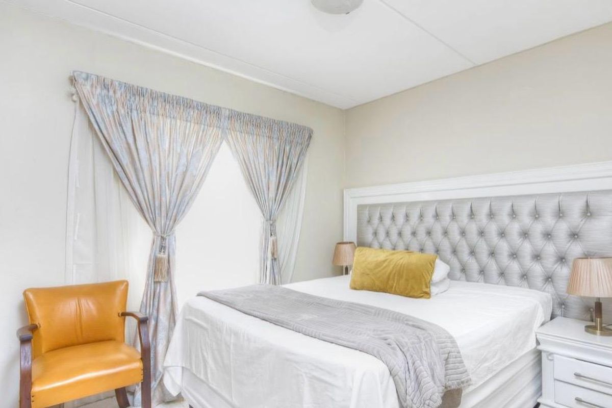 A well-maintained bedroom featuring neutral wall tones, a built-in wardrobe, and a large window with classic drapery.