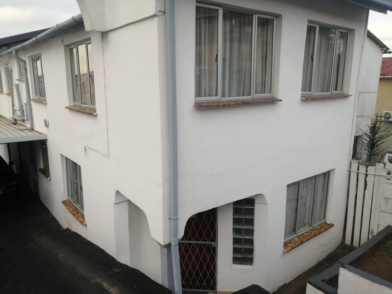 A two-story exterior view of the property featuring white painted walls, aluminium window frames, and a glass block accent near the entrance.