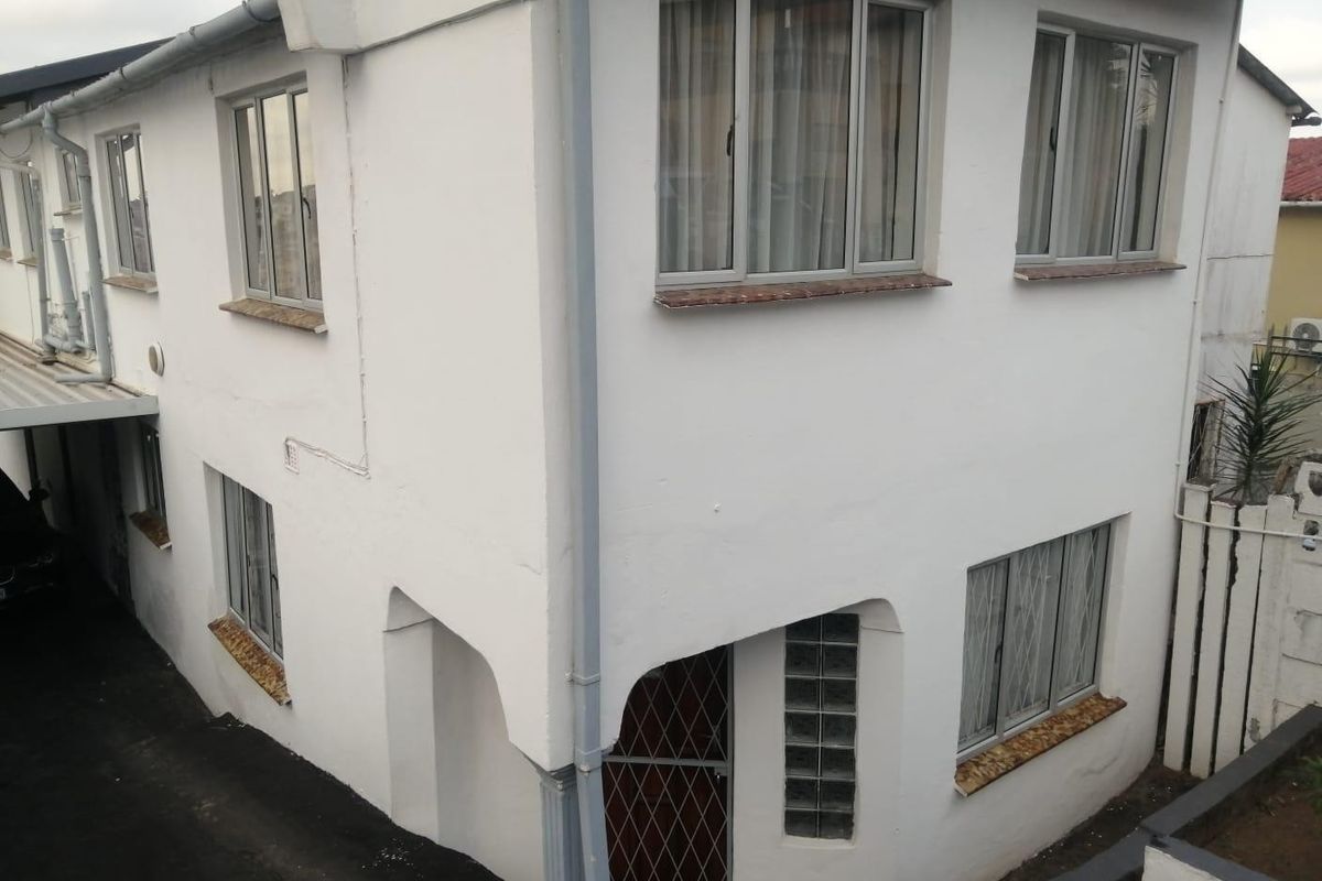 A two-story exterior view of the property featuring white painted walls, aluminium window frames, and a glass block accent near the entrance.