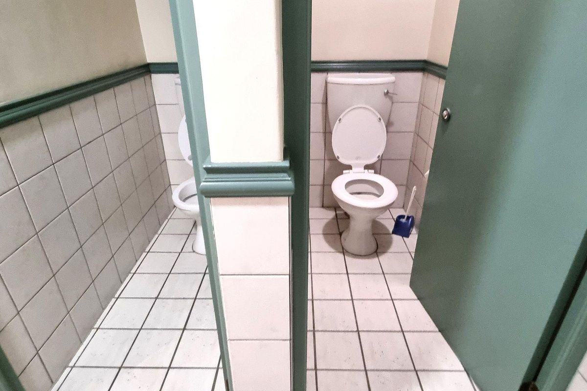 A functional office restroom featuring two partitioned toilet stalls with tiled walls and flooring.