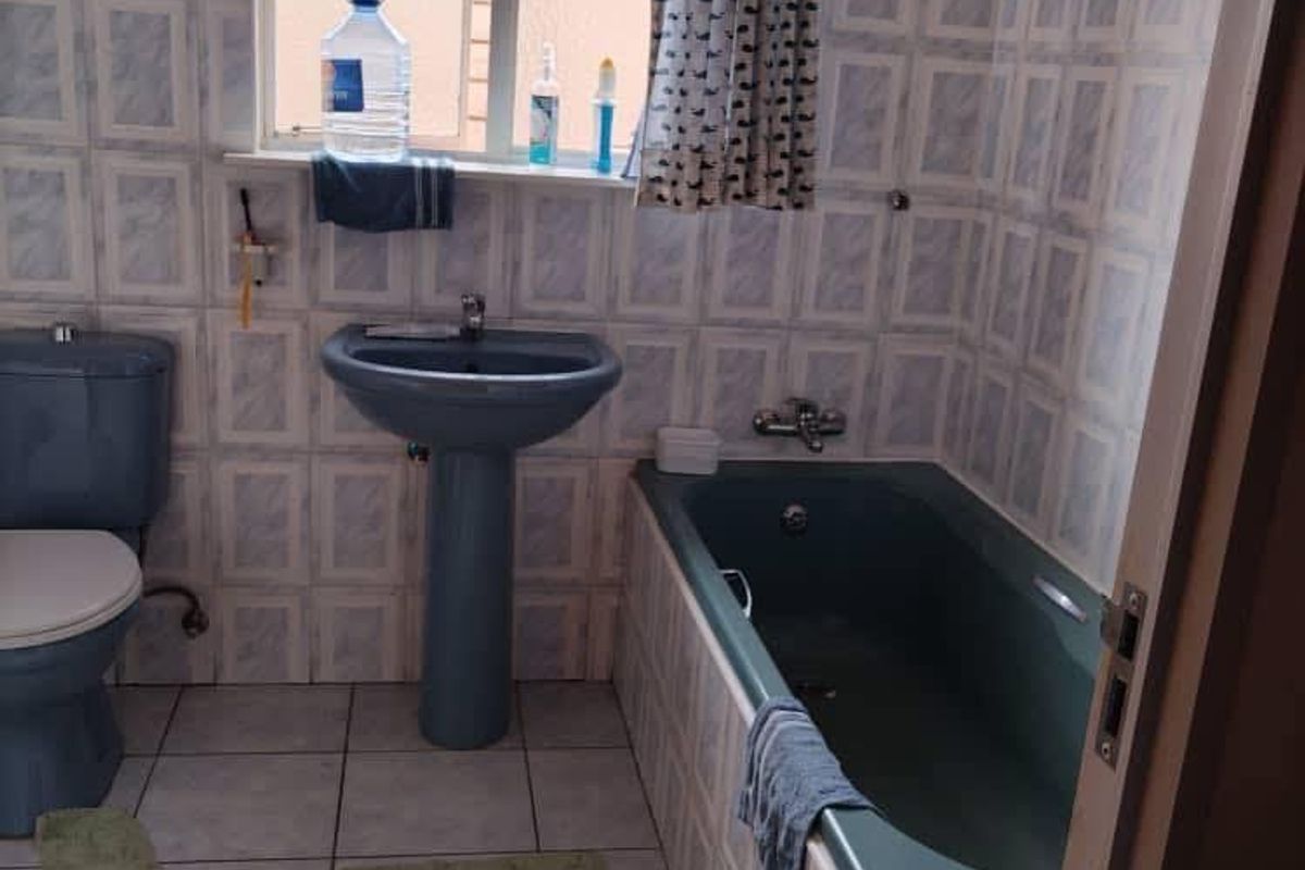 A dated bathroom featuring a blue pedestal basin, matching toilet, and built-in bathtub with full-height wall tiling and tiled flooring.