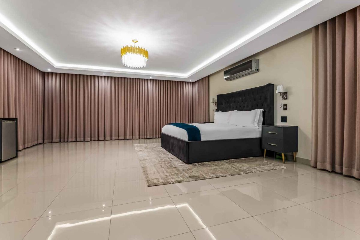 Spacious bedroom featuring polished tile flooring, recessed ceiling lighting, full-length curtains, and a wall-mounted air conditioning unit.