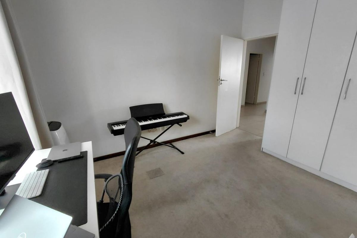 A bedroom featuring built-in cupboards and carpeted flooring, currently utilized as a home office and music space.