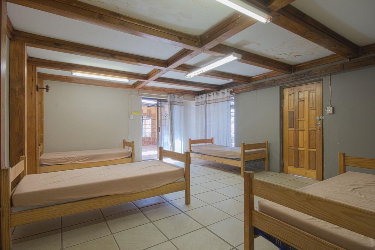 A spacious bedroom featuring exposed timber ceiling beams, tiled flooring, and direct access to an outdoor patio area.