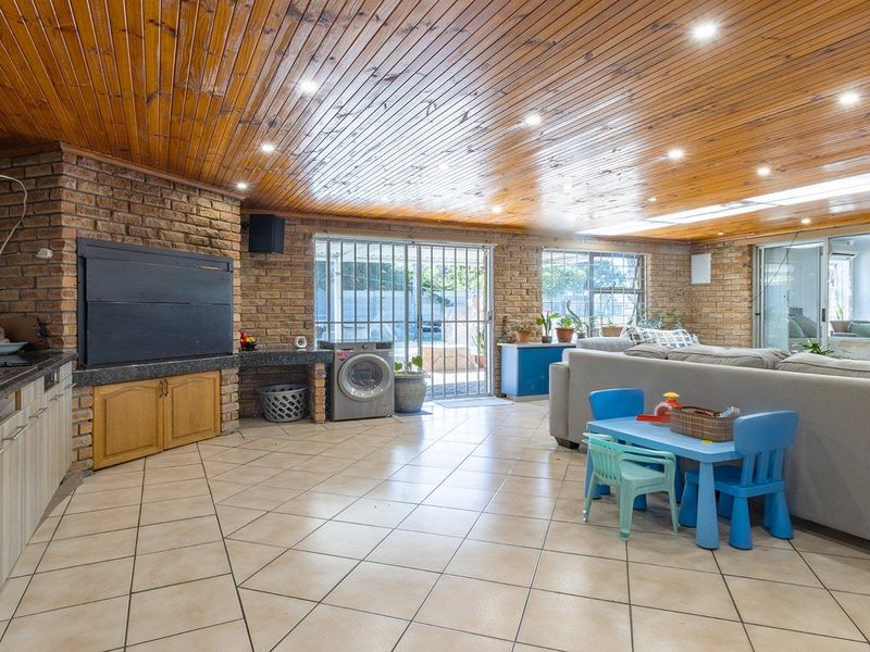 Spacious open-plan living area featuring exposed brick walls, a timber ceiling, built-in braai, and direct access to the outdoor area through sliding doors.