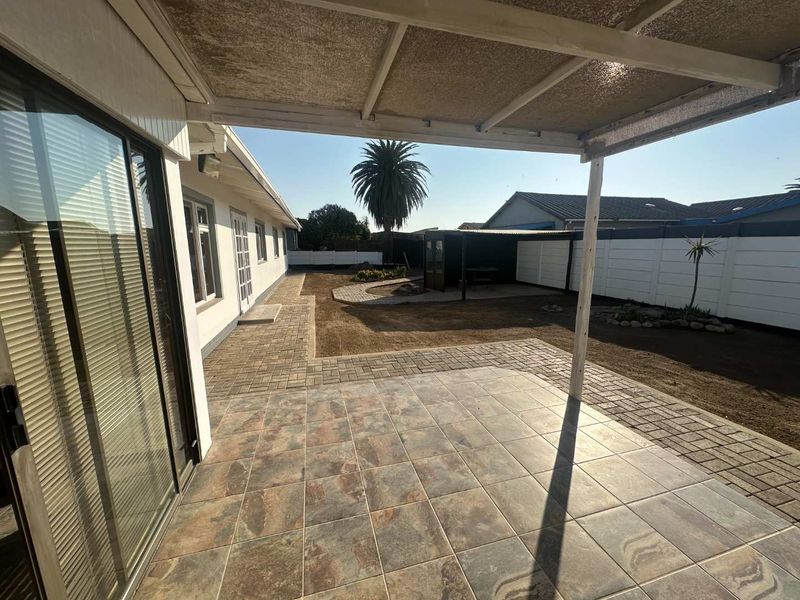 A covered patio area with tiled flooring leading out to a paved garden path and a fenced backyard.
