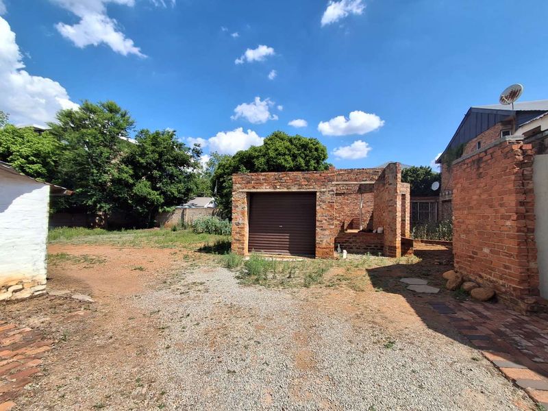 Rear exterior view showing an unfinished brick garage structure with a roller shutter door, set within a large, unlandscaped yard area.
