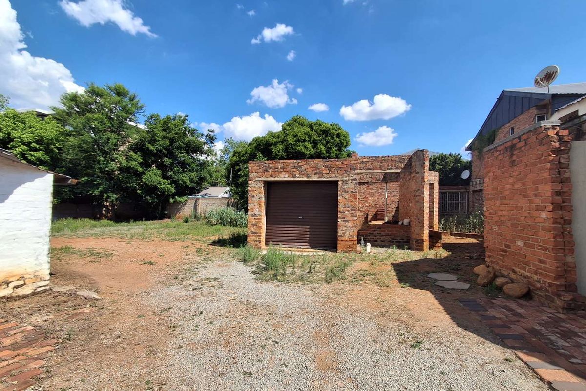 Rear exterior view showing an unfinished brick garage structure with a roller shutter door, set within a large, unlandscaped yard area.